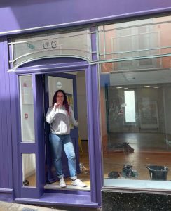 Aimi stands in the doorway of her new shop in blue jeans and a white top. She is holding the key.